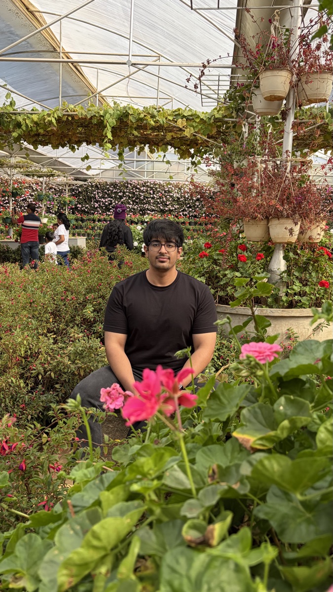Saksham Bhardwaj seated among flowers in a greenhouse